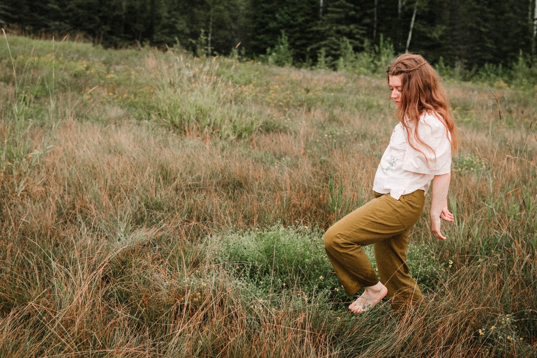 dancer and embripdery artist, Heather Annis, dances in a meadow in Two Harbors, Minnesota. She wear green pants and a pink embroidered shirt.